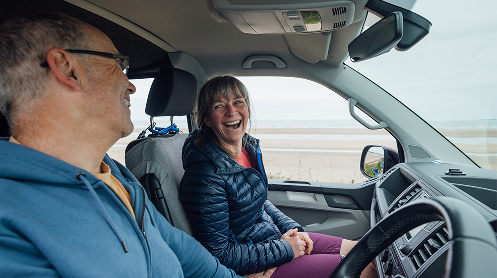 A mature couple wearing sports clothing on an overcast day in Alnmouth, Northumberland, Northeastern England. They are sitting in their campervan by the sea and share a laugh.